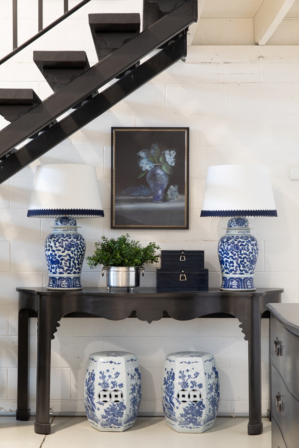 4 leg dark console table in entryway styled with blue lamps, boxes and a pot plant