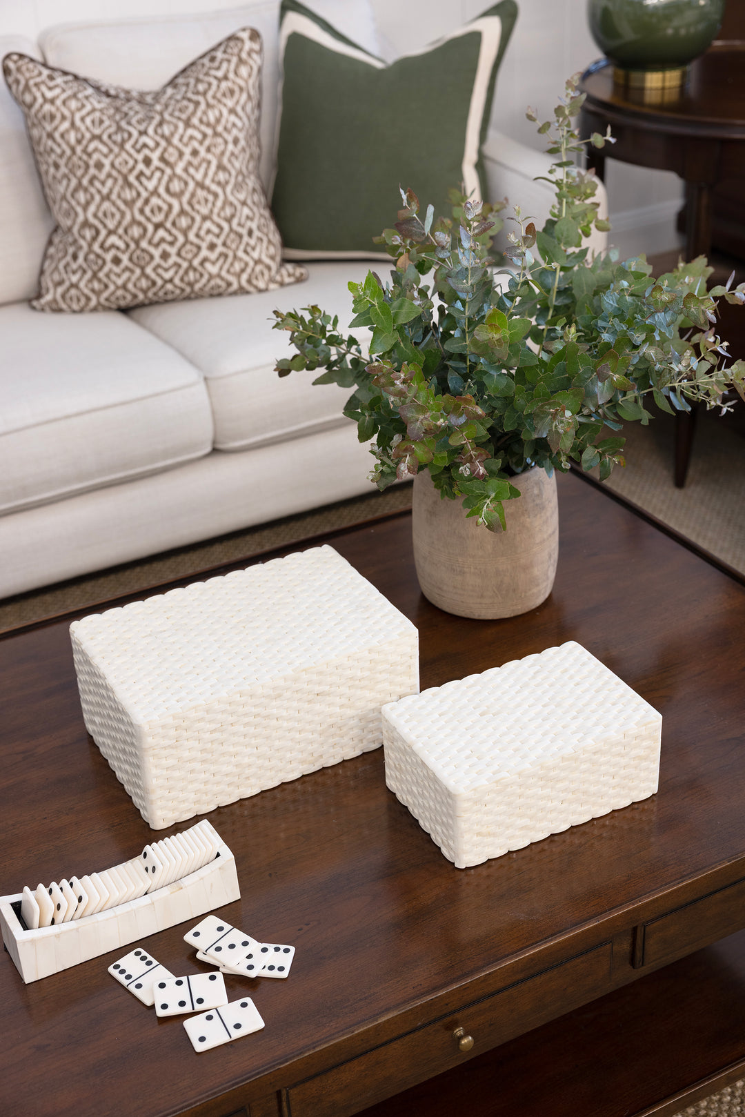 Decorative boxes on a coffee table with a vase of flowers and dominoes in a living room setting.