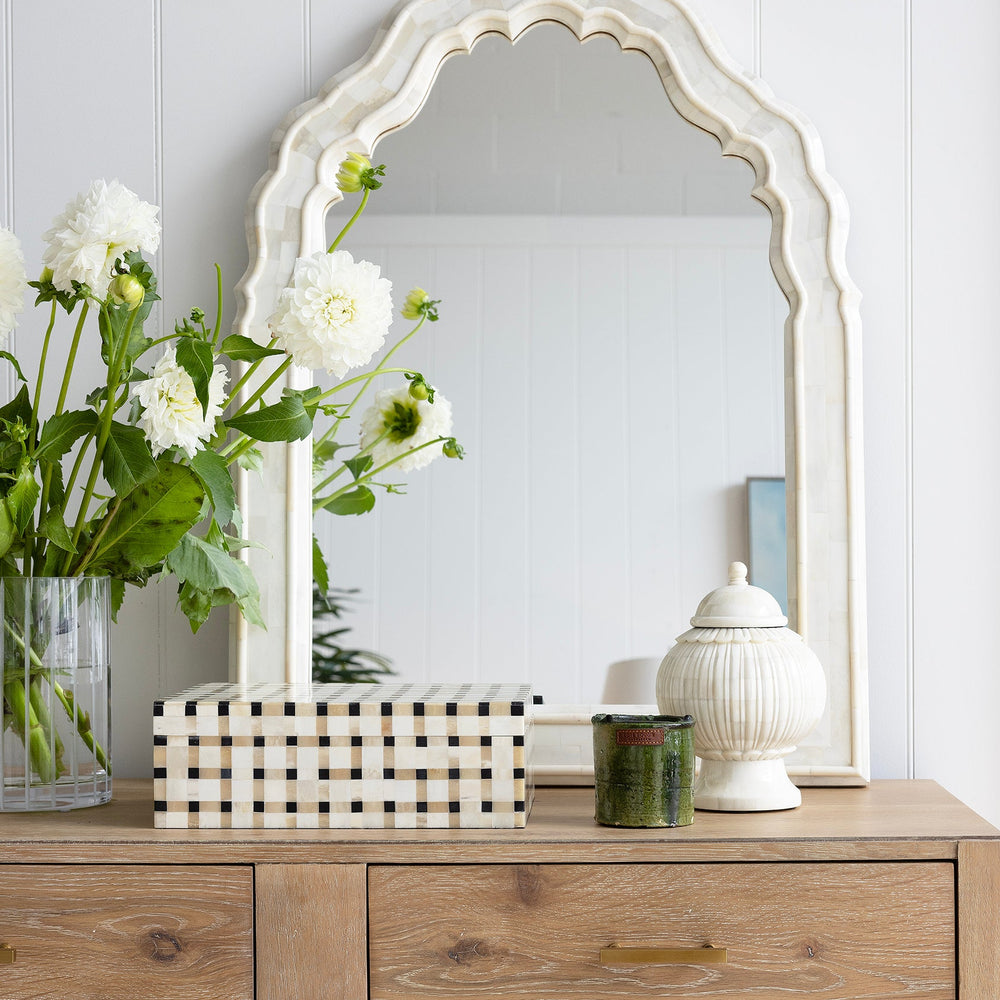 Timber console with decorative items and a large scalloped bone mirror against a white wall.