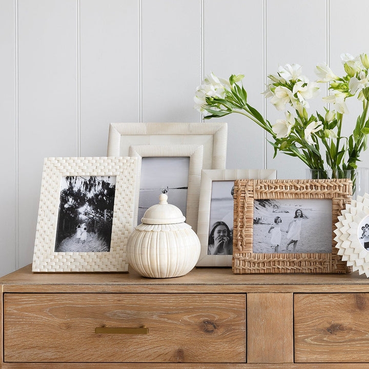 Wooden dresser with decorative items including framed photos and a vase of flowers against a white wall.