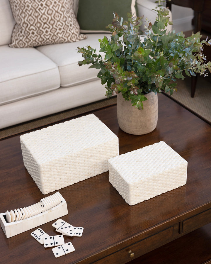 Decorative boxes on a coffee table with a vase of flowers and dominoes in a living room setting.