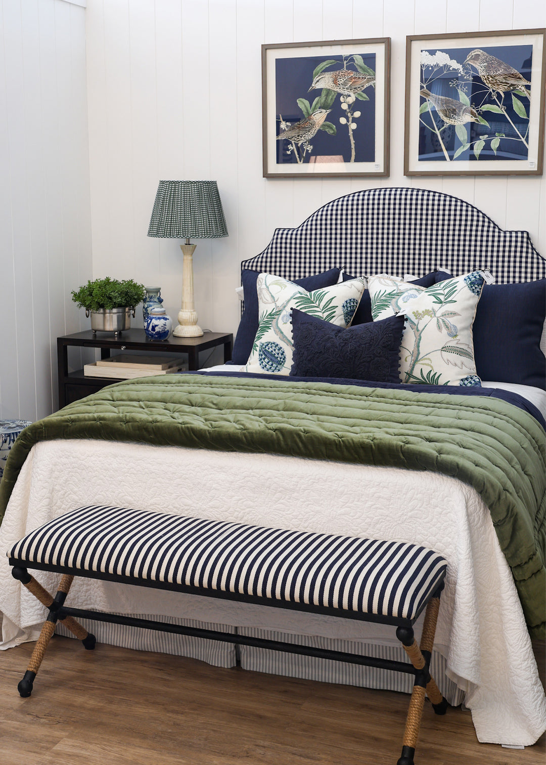 Bedroom with a bed featuring green bedding and decorative pillows, a striped bench at the foot of the bed, and framed artwork on the wall.