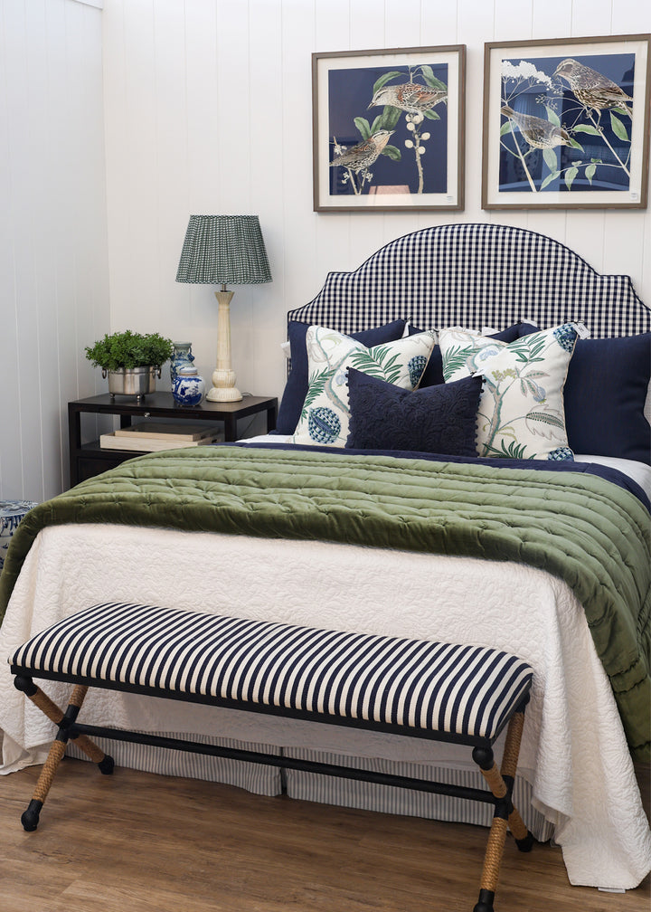 Bedroom with a bed featuring green bedding and decorative pillows, a striped bench at the foot of the bed, and framed artwork on the wall.