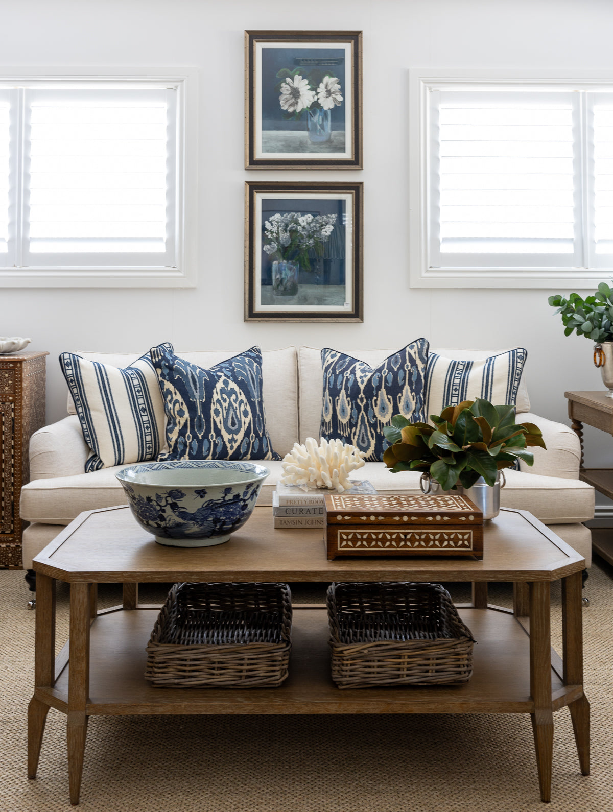 Buena Vista cushion styled in a living room with an indigo ikat cushion on a neutral sofa. A styled coffee table is placed in front and two indigo floral artworks sit above the sofa on the back wall.