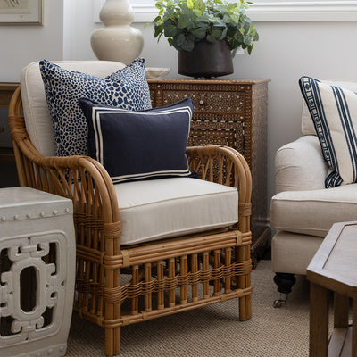 Side image of cape cod arm chair with a porcelain stool sitting beside it. The chair is styled with a navy animal print cushion and a small navy lumbar cushion. The chair sits in front of a bone inlay and teak timber cabinet. 