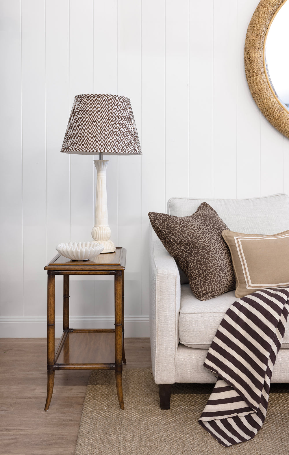 Living room with a side table, lamp, and sofa with pillows and a blanket.