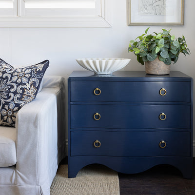 Image of Navy Claire Chest styled next to a neutral sofa with a navy embroidered cushion. The chest is styled  with an oval ruffled marble bowl and faux fittonia greenery on top, figure study artwork hanging on wall above.