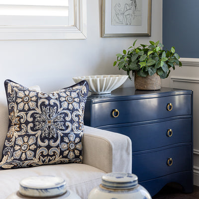 Image of Navy Claire Chest styled next to a neutral sofa with a navy embroidered cushion. The chest is styled  with an oval ruffled marble bowl and faux fittonia greenery on top, figure study artwork hanging on wall above.