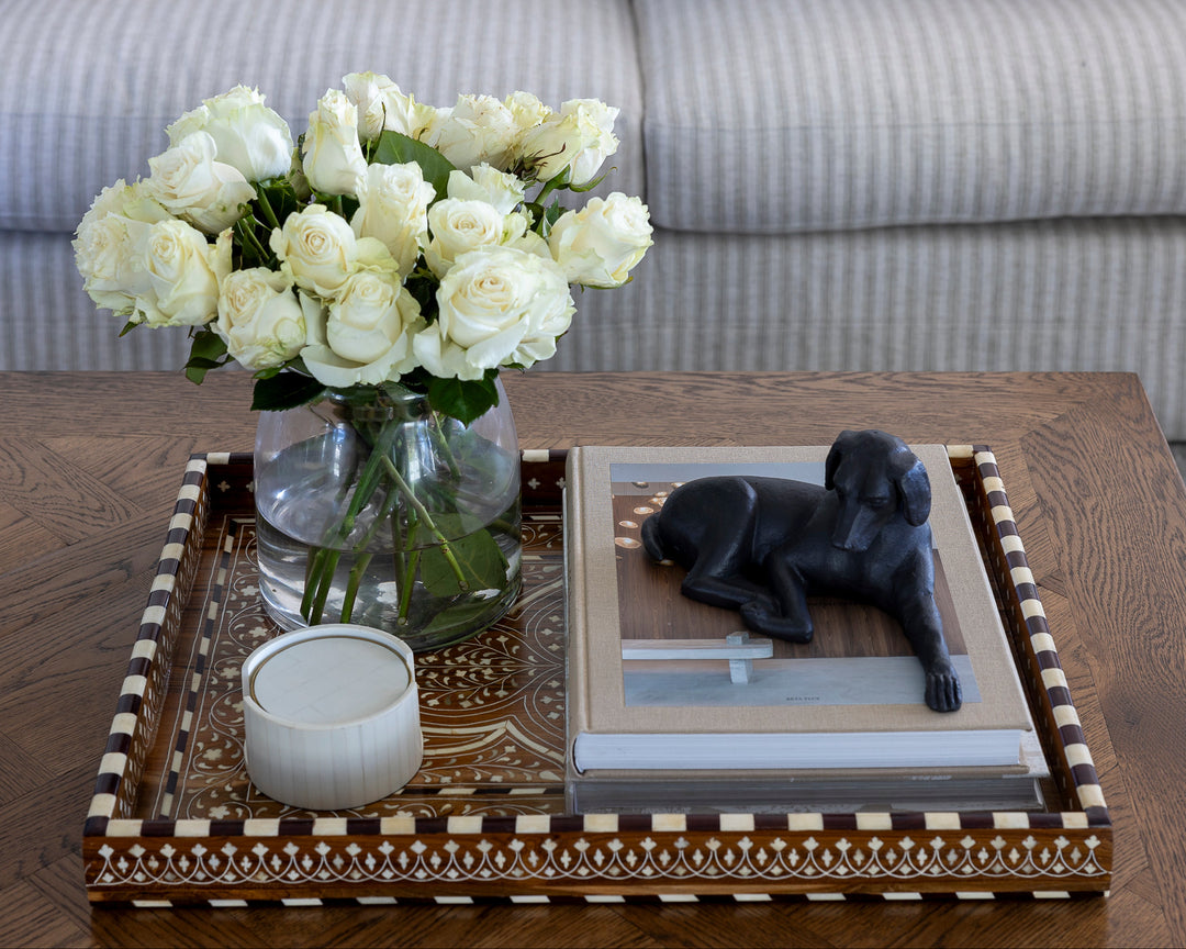 Decorative coffee table with white roses, a candle, and a photo of a dog in a living room.