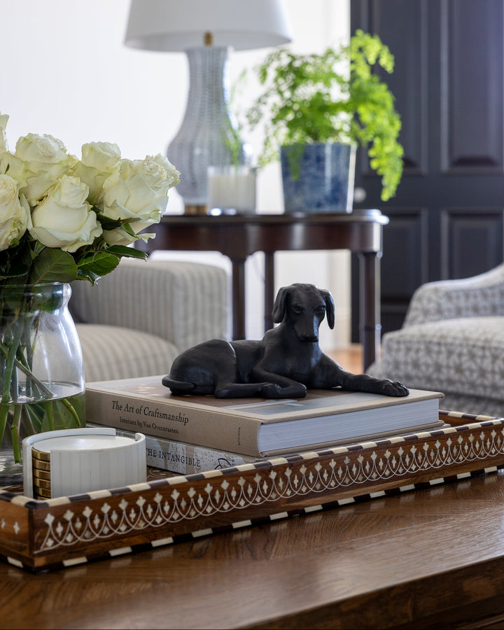 Decorative tray with a black dog figurine, books, and flowers on a wooden surface.