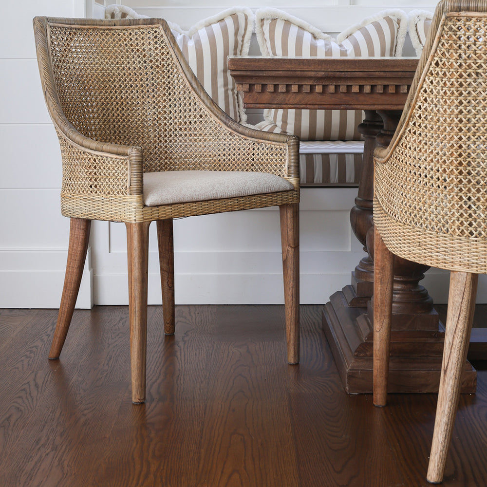 Woven rattan dining chair with a mango wood dining table and a bench seat with striped cushions behind.