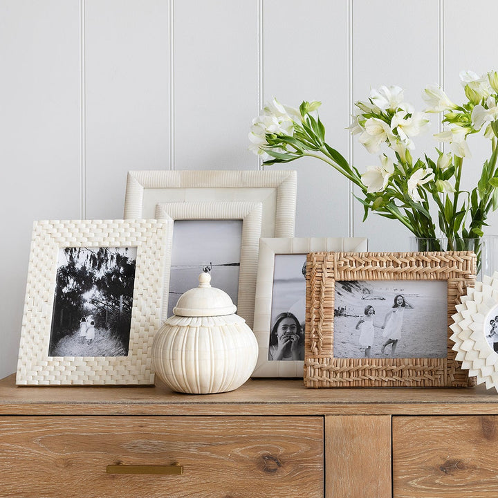 Wooden dresser with decorative items including framed photos and a vase of flowers against a white wall.