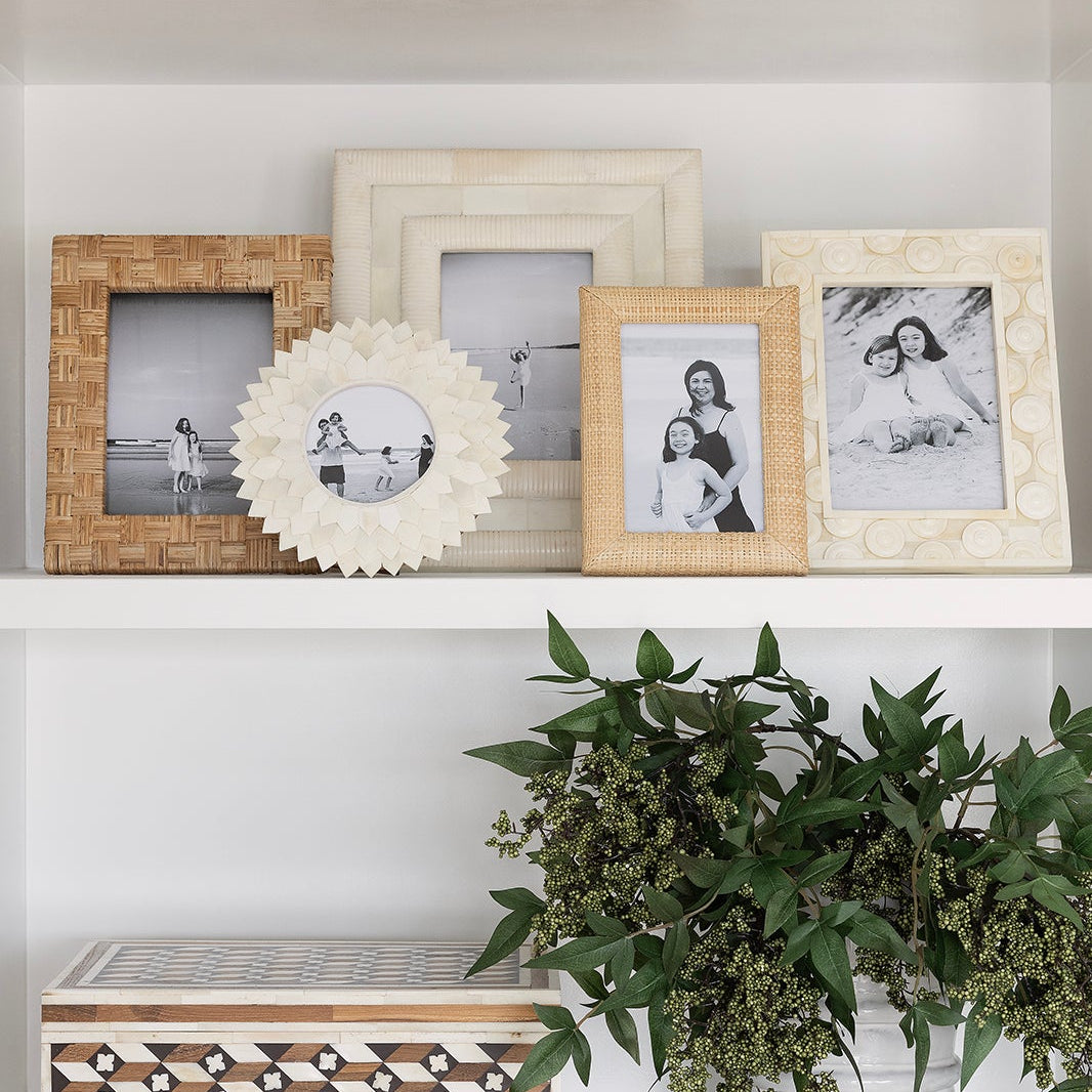Decorative shelf with picture frames, a plant, and a decorative item against a checkered wall.