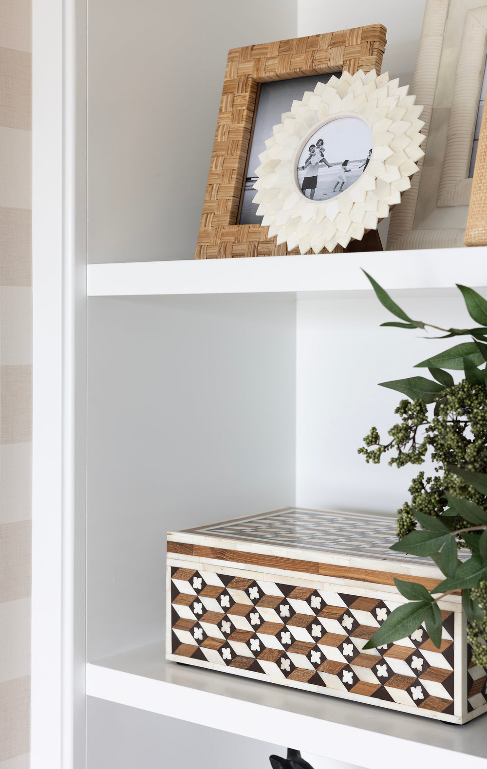 Decorative box with geometric pattern on a shelf with framed pictures and a plant.