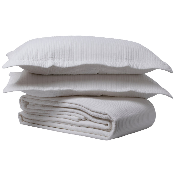 Folded bedspread in white with two pillows stacked on top.
