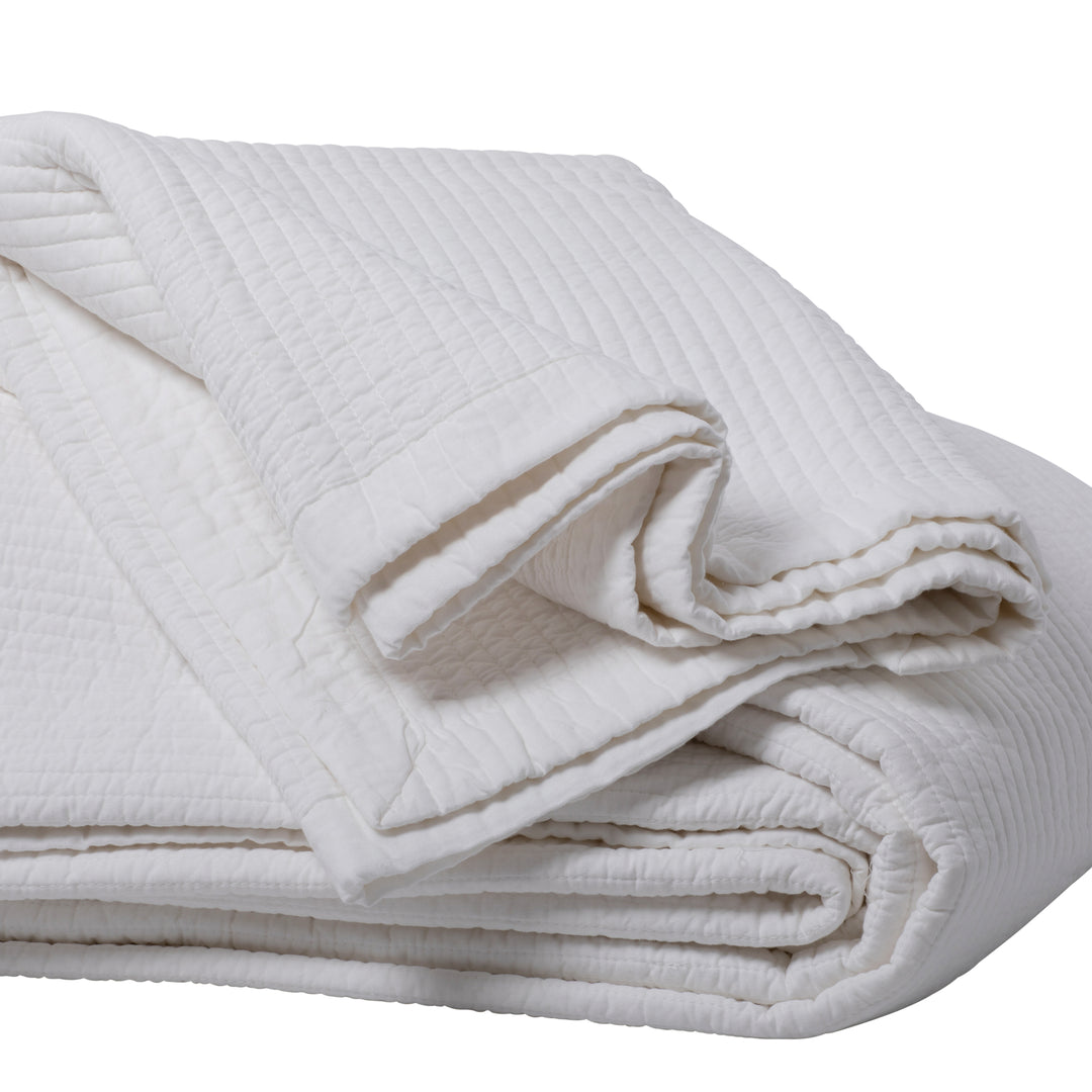 Close up image of folded white quilt on a white background