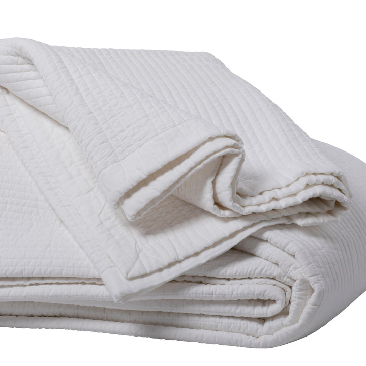 Close up image of folded white quilt on a white background