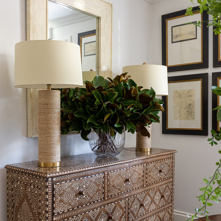 Two finn lamps styled on a timber and bone inlay chest of drawers with a large vase of faux magnolia leaves in the centre. 