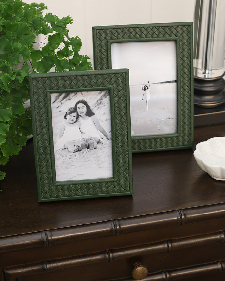 Two green photo frames on a wooden surface with containing black and white photos of children.