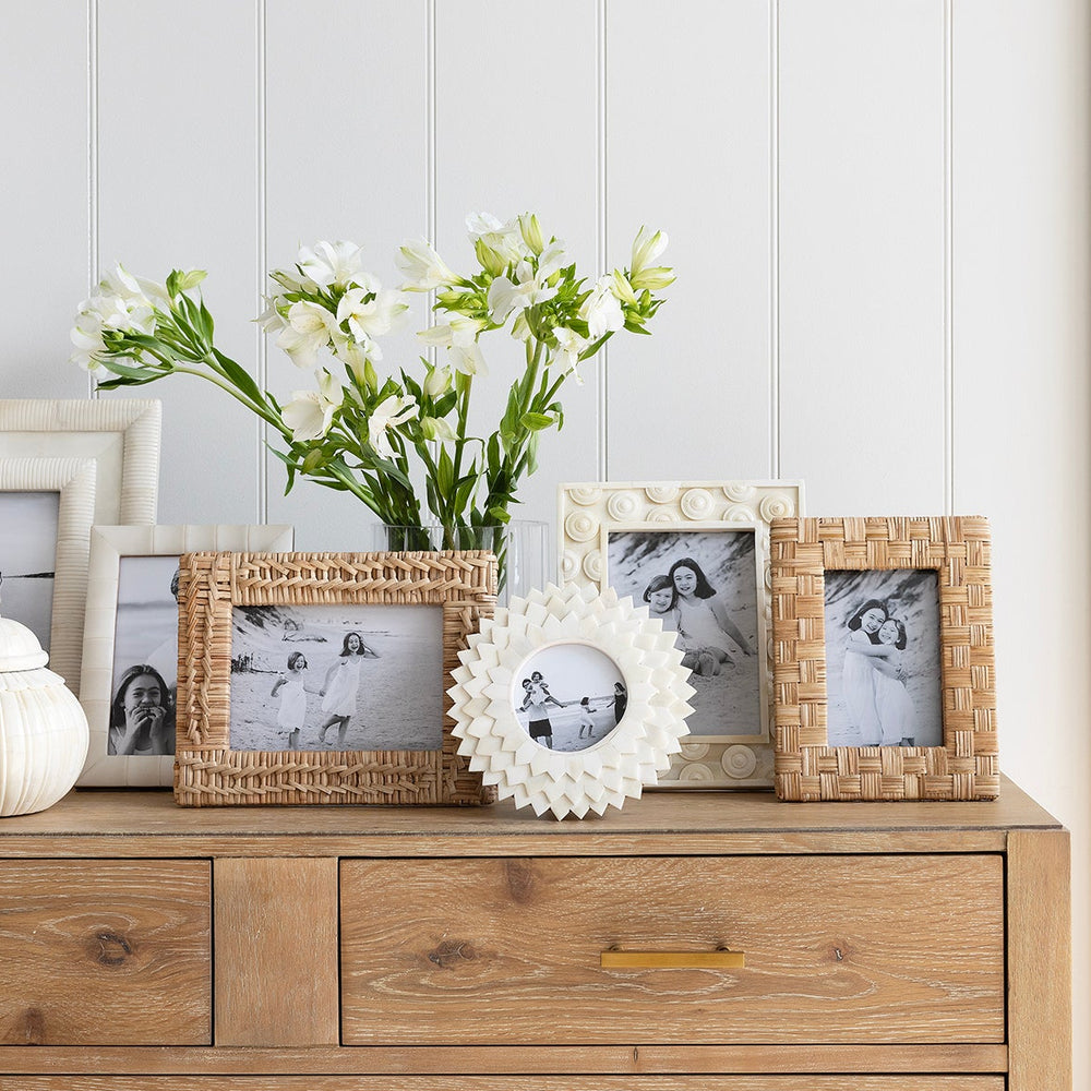 Wooden dresser with decorative items including framed photos and a vase of flowers against a white wall.