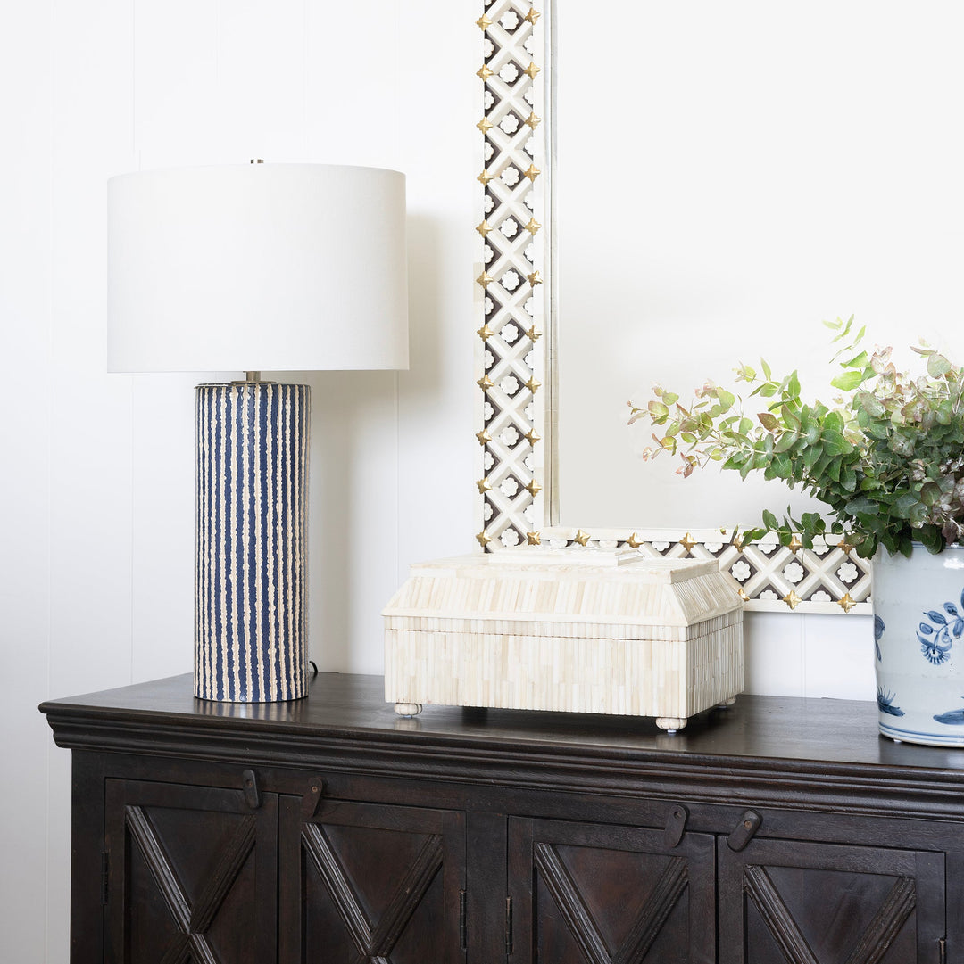 Decorative sideboard with a lamp, box, and plant against a white wall.