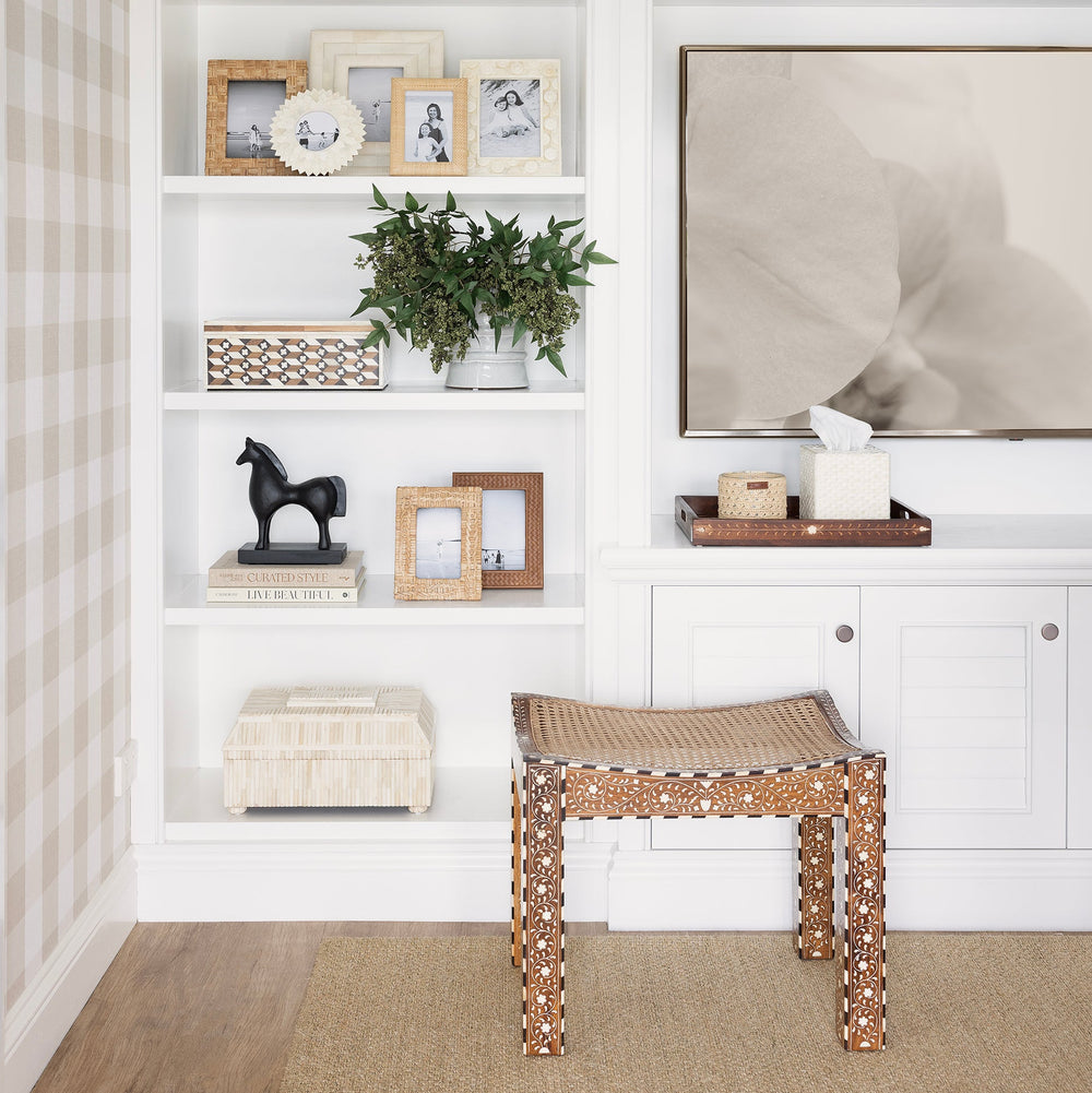 Products styled in white bookshelf with ottoman sitting in front