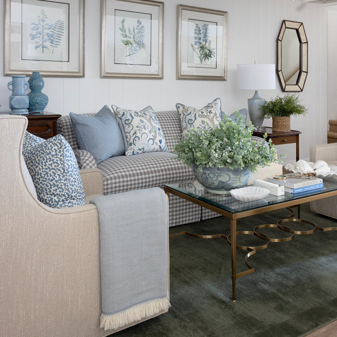 Blue patterned cushions on a gingham lounge in a layered living space with glass coffee table and artwork.