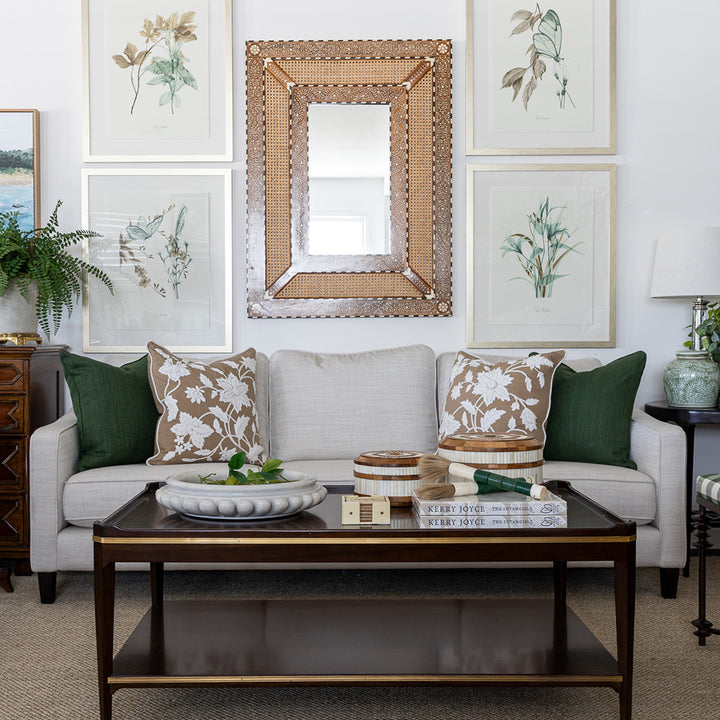 Image of maddox coffee table styled in front of a neutral sofa with green and caramel cushions. The coffee table is styled on top with a large marble bowl filled with limes, a set of cream coasters, teak and bone inlay round boxes and a stack of books topped with ornamental paint brushes. Behind the coffee table is a large rattan and bone inlay decorative mirror on the wall. 