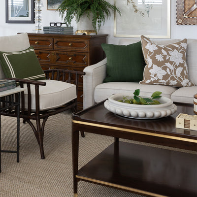 Image of maddox coffee table styled in front of a neutral sofa with green and caramel cushions. The coffee table is styled on top with a large marble bowl filled with limes, a set of cream coasters, teak and bone inlay round boxes and a stack of books topped with ornamental paint brushes. Behind the coffee table is a large rattan and bone inlay decorative mirror on the wall.