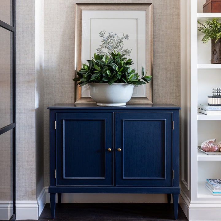 Navy Toulon Hall chest styled next to a built in bookcase. A large white bowl with faux sweet leaf greenery and an artwork placed behind. 