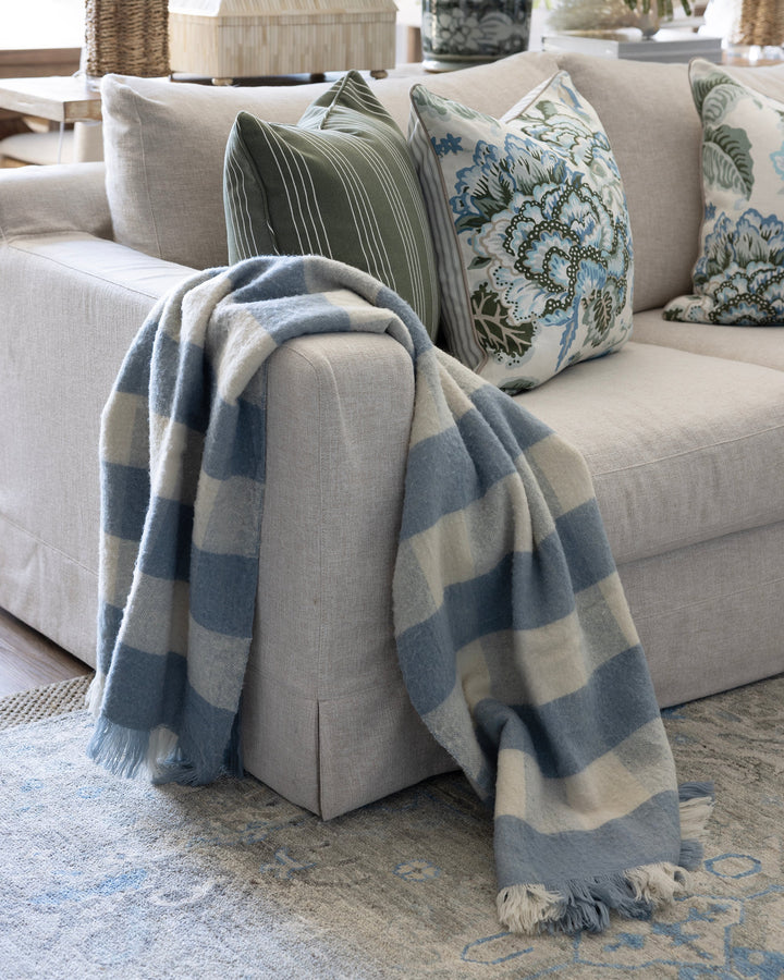 A light gray sofa in a bright living room styled with blue and cream striped throw blankets and patterned pillows.