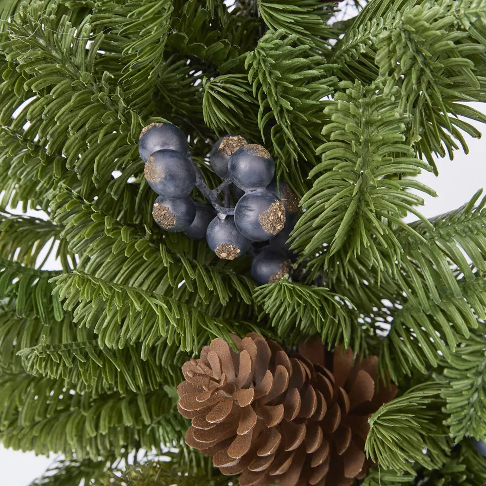 Close-up of artificial greenery with blue berries and pine cones on a white background