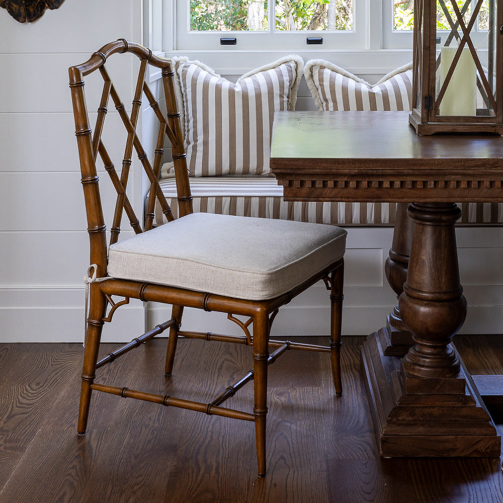 Image of Ralph Dining Chair at a beach house dining room. Shown with a wooden table and a striped cushion bench seat beside it. The chair sits at the end of the table.