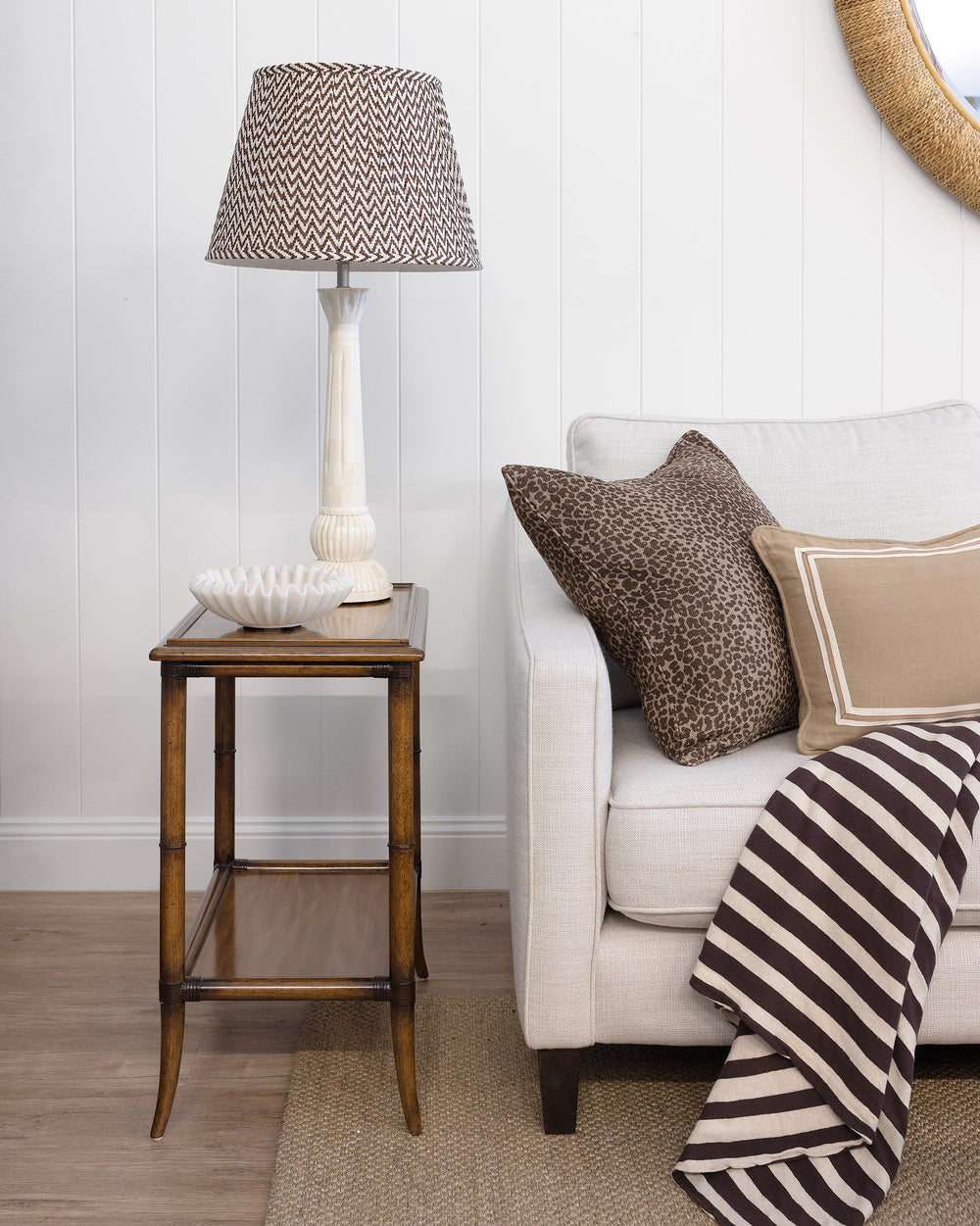 Living room with a side table, lamp, and sofa with pillows and a blanket.