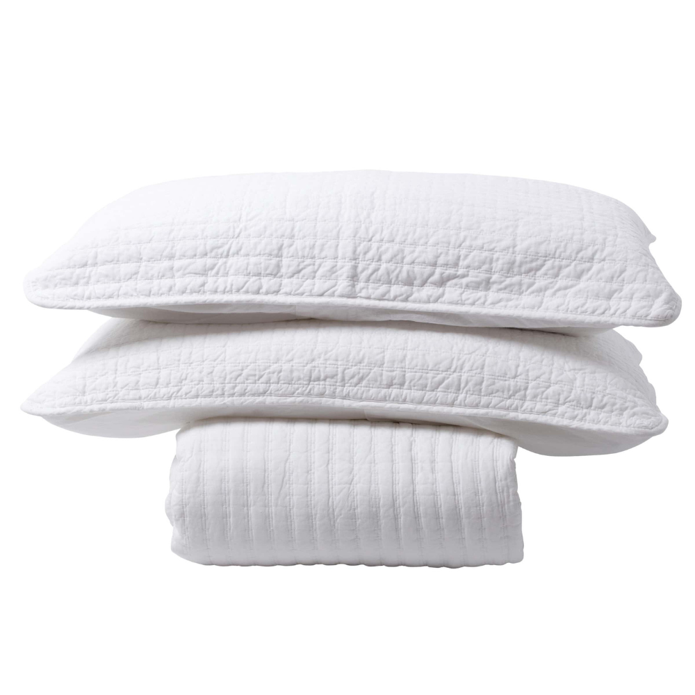 White bedspread with two pillowcases stacked on top on white background.