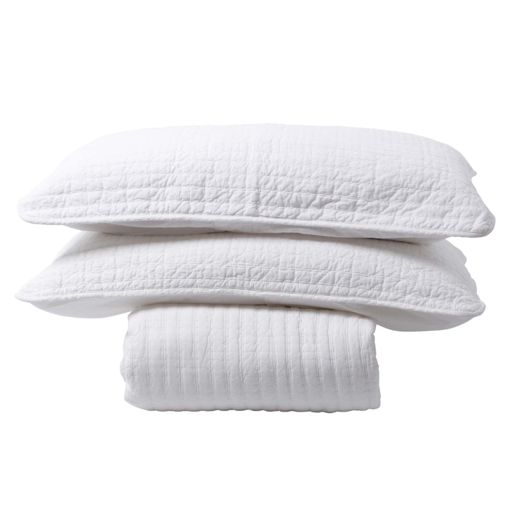 White bedspread with two pillowcases stacked on top on white background.