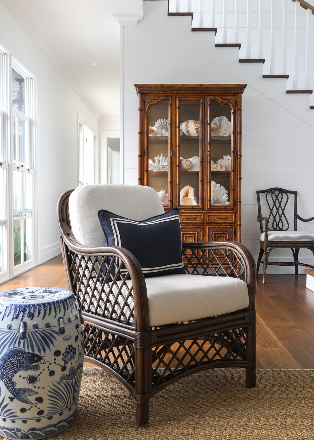 Wicker chair with white cushion and navy pillow in a room with wooden floor and staircase.