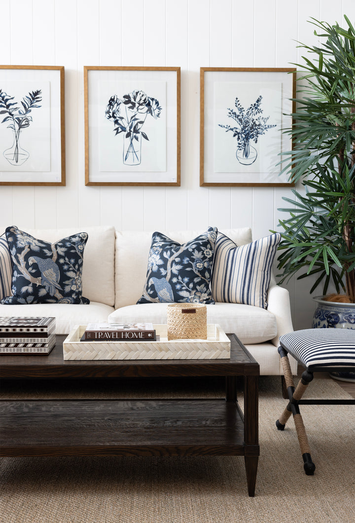 Living room with a white sofa, decorative pillows, a wooden coffee table, and framed botanical prints on the wall.