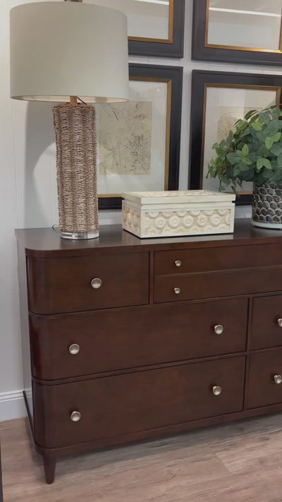 Video of styled Eleanora dresser. On the dresser there are two table lamps a bone inlay box and a faux greenery plant. Four images on the wall behind. 